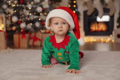 Photo of Cute baby wearing Santa's elf clothes in room with Christmas decorations