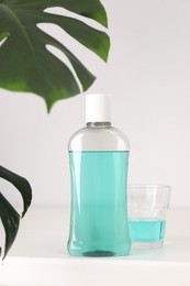 Photo of Bottle of mouthwash and glass on white table in bathroom