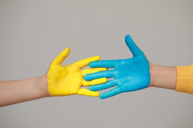 Photo of Little girl and boy with hands painted in Ukrainian flag colors on light grey background, closeup. Love Ukraine concept