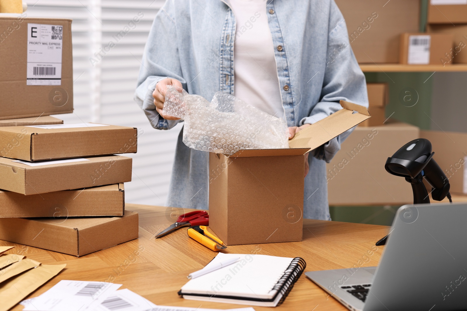 Photo of Post office worker packing parcel at wooden table indoors, closeup