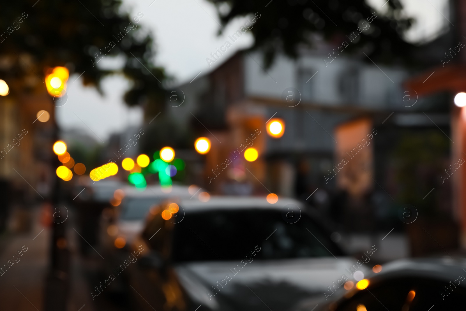 Photo of Blurred view of city street with parked cars in evening