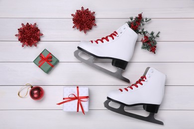 Pair of ice skates, Christmas decor and gift boxes on white wooden background, flat lay