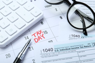 Photo of Calendar with date reminder about tax day, documents, glasses, pen and calculator, closeup