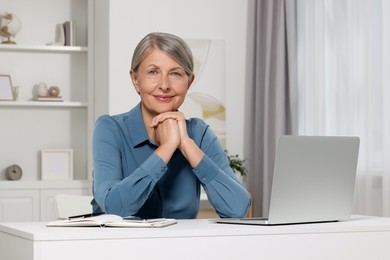 Photo of Beautiful senior woman near laptop at white table indoors
