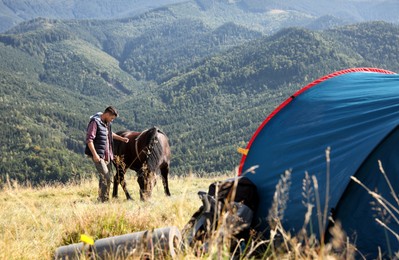 Photo of Man and horse near camping tent in mountains
