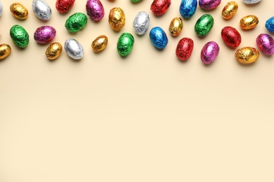 Chocolate eggs wrapped in colorful foil on beige background, flat lay. Space for text