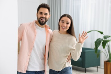 Photo of Happy couple waving near white wall at home. Invitation to come in room