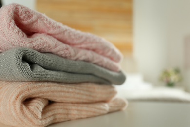 Stack of knitted sweaters on white table indoors, closeup