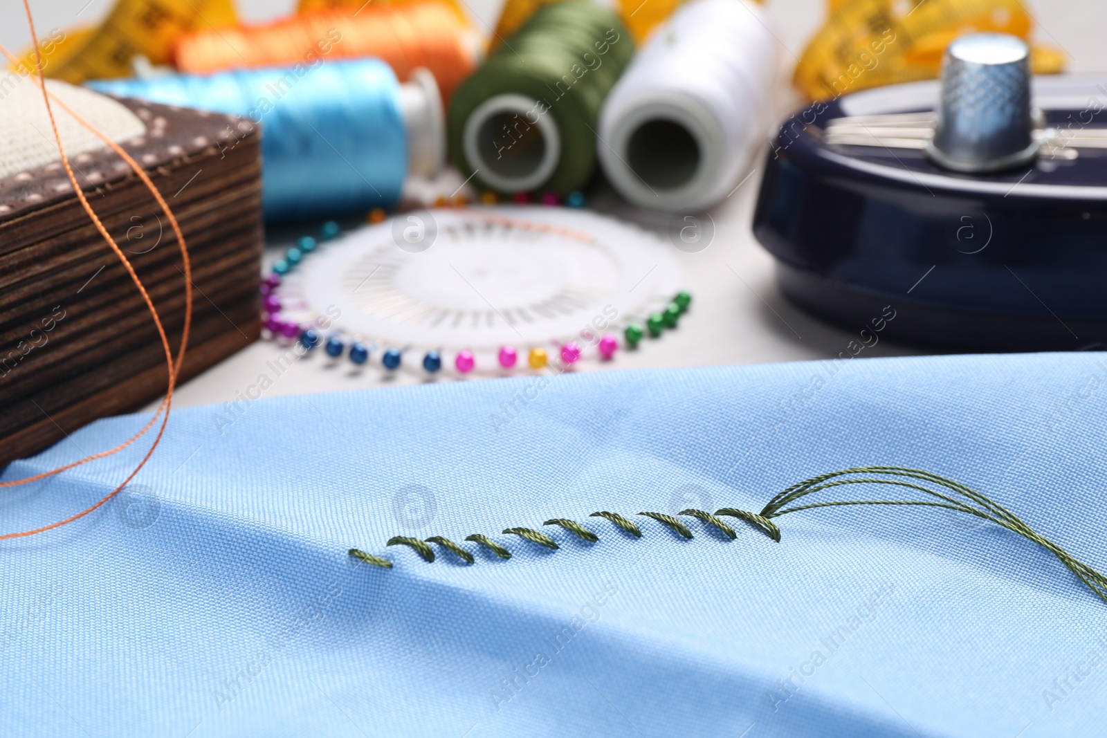 Photo of Light blue cloth with sewing thread and stitches on table, closeup