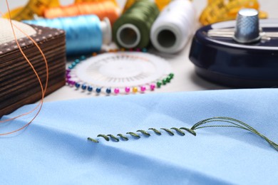 Light blue cloth with sewing thread and stitches on table, closeup