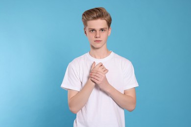 Teenage boy suffering from pain in hand on light blue background. Arthritis symptom