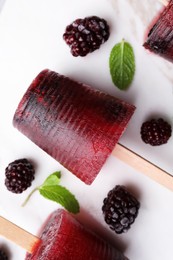 Photo of Tasty blackberry ice pops on white marble table, flat lay. Fruit popsicle