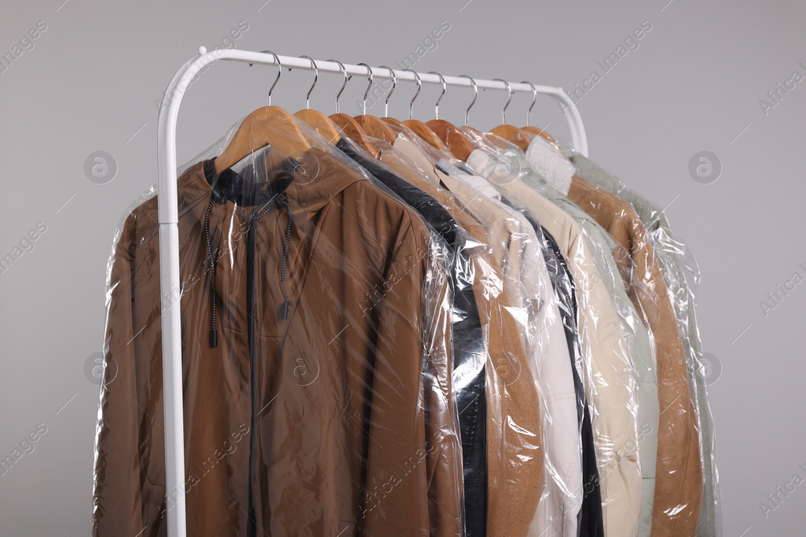 Photo of Dry-cleaning service. Many different clothes in plastic bags hanging on rack against grey background