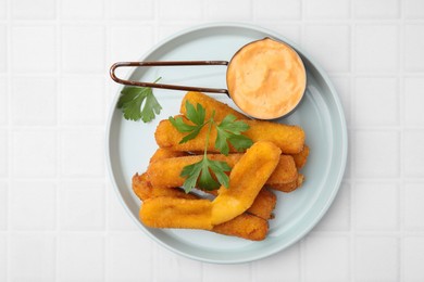 Tasty fried mozzarella sticks served with sauce and parsley on white tiled table, top view