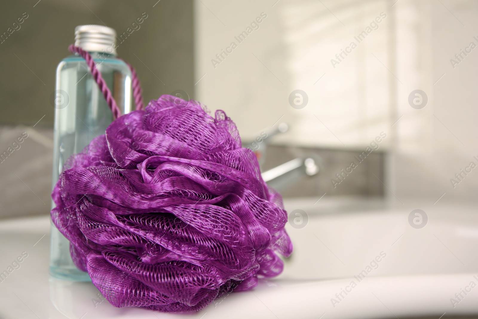 Photo of Purple shower puff and bottle of body wash gel on sink in bathroom, closeup. Space for text