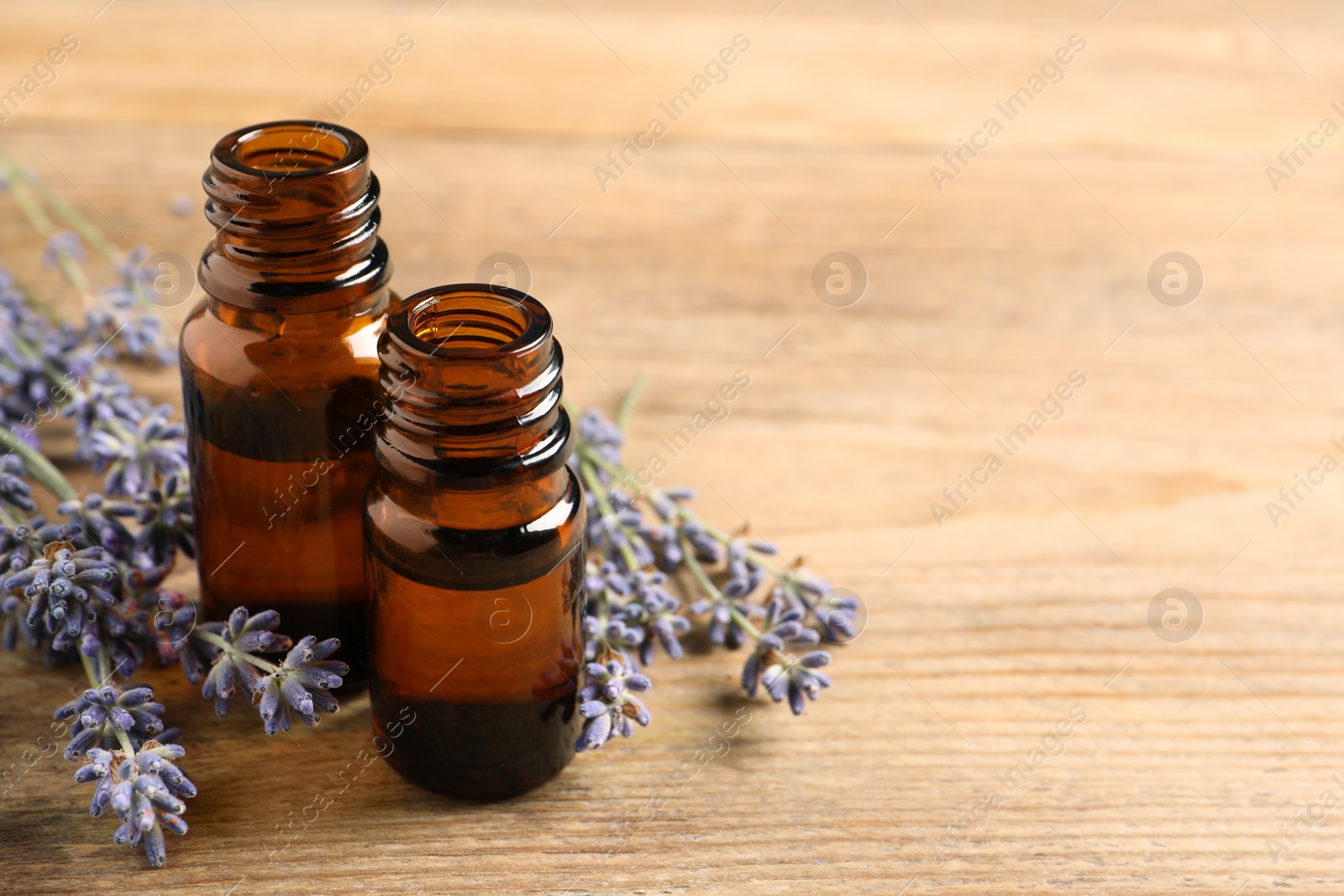 Photo of Essential oil and lavender flowers on wooden table, closeup. Space for text