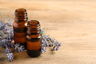 Essential oil and lavender flowers on wooden table, closeup. Space for text