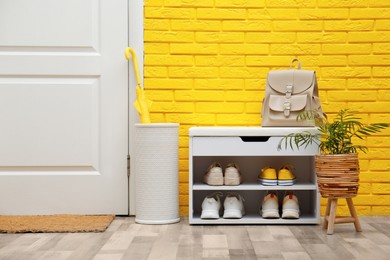 Photo of Shelving unit with shoes near yellow brick wall in hallway