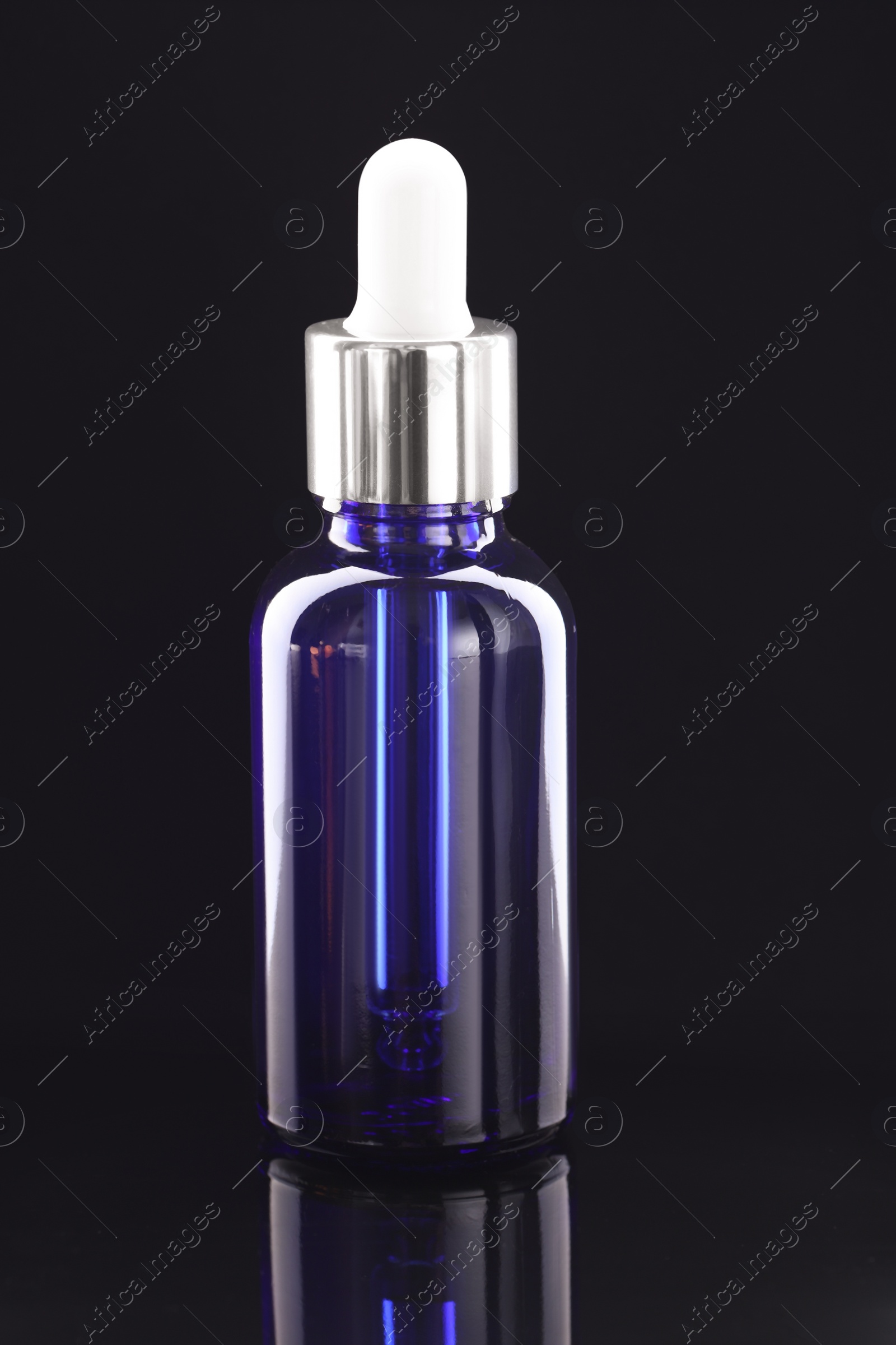 Photo of Tincture in bottle on mirror table against dark background