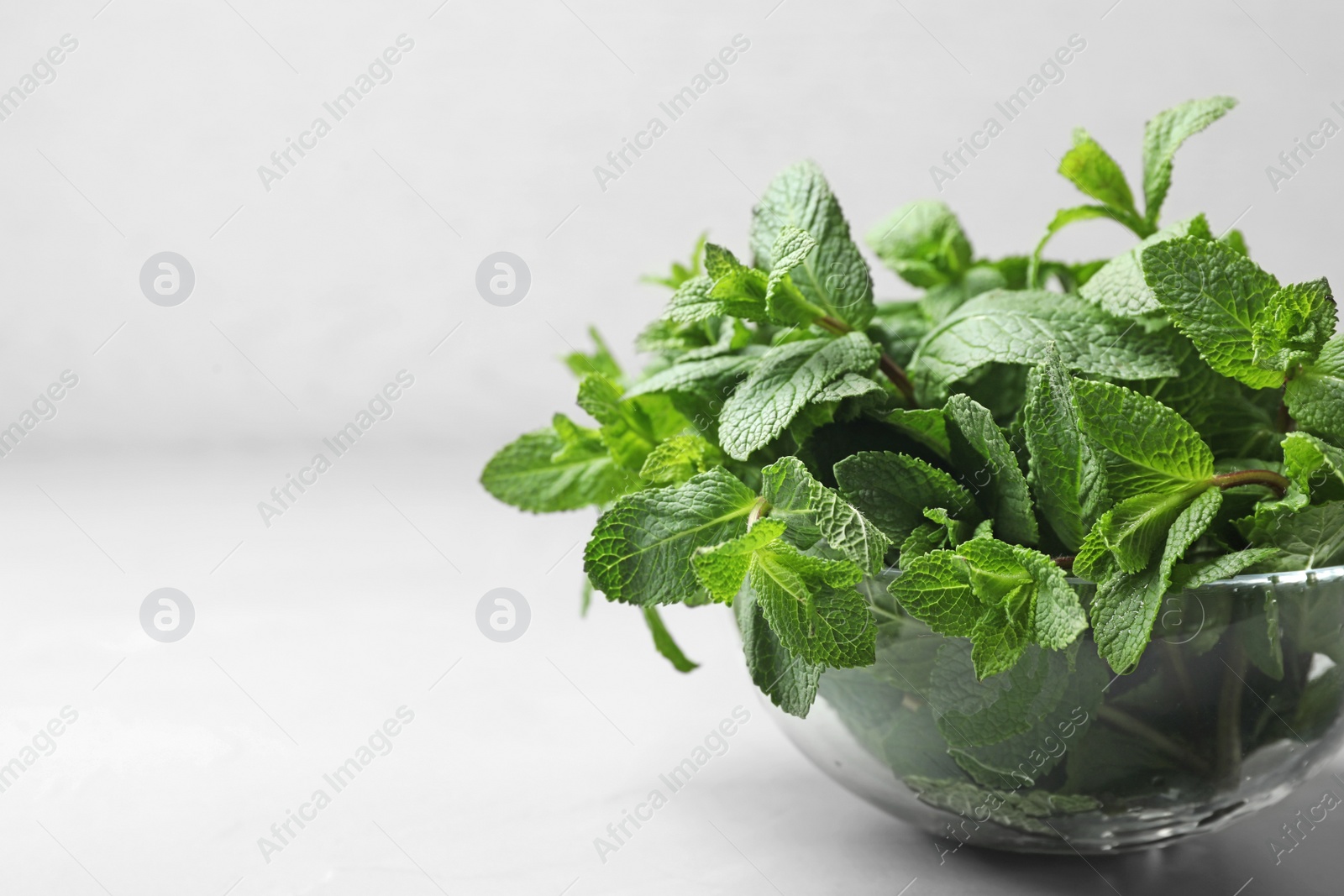 Photo of Glass bowl with fresh green mint on table. Space for text