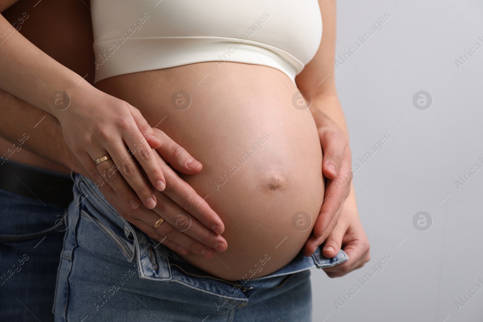 Photo of Man touching his pregnant wife's belly on light background, closeup