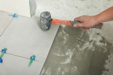 Worker with rubber hummer installing tiles indoors , closeup