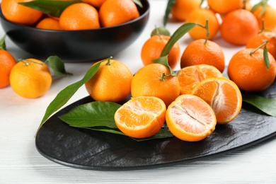 Photo of Fresh ripe tangerines with green leaves on white wooden table