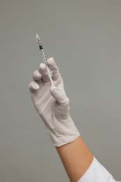 Doctor holding medical syringe on grey background, closeup