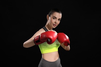 Photo of Beautiful woman in boxing gloves training on black background