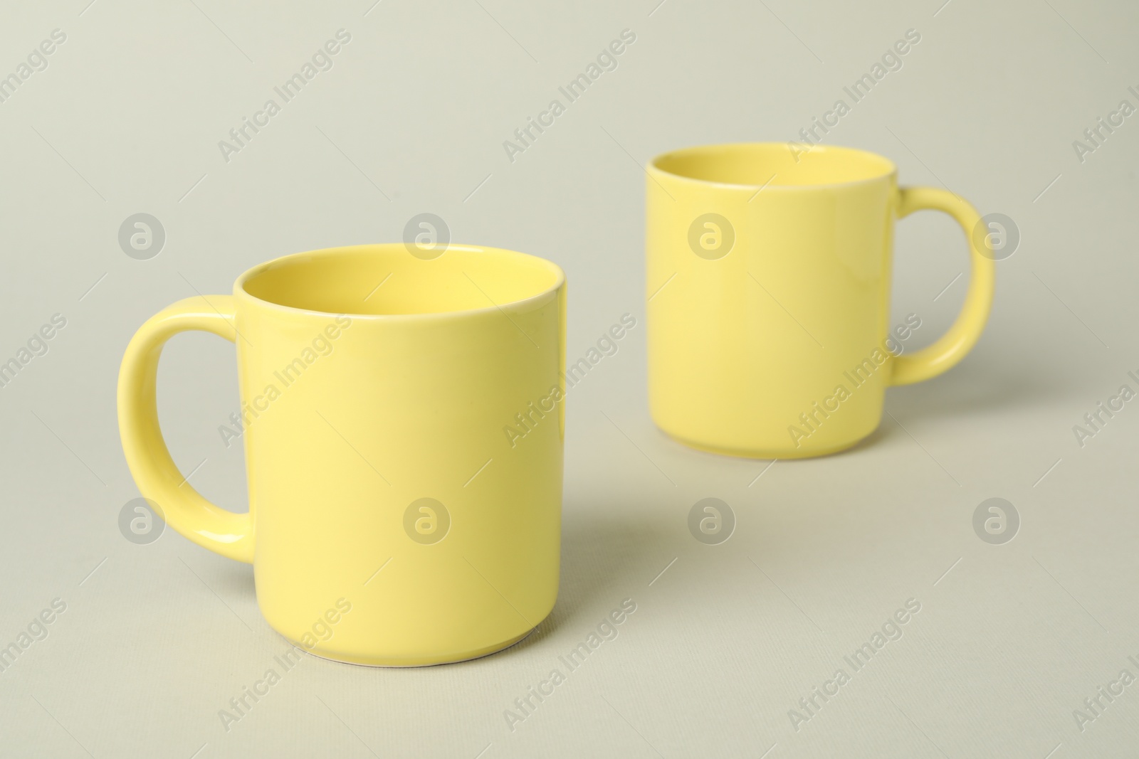 Photo of Two yellow ceramic mugs on light grey background