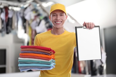 Image of Happy courier holding folded clothes and clipboard in dry-cleaning