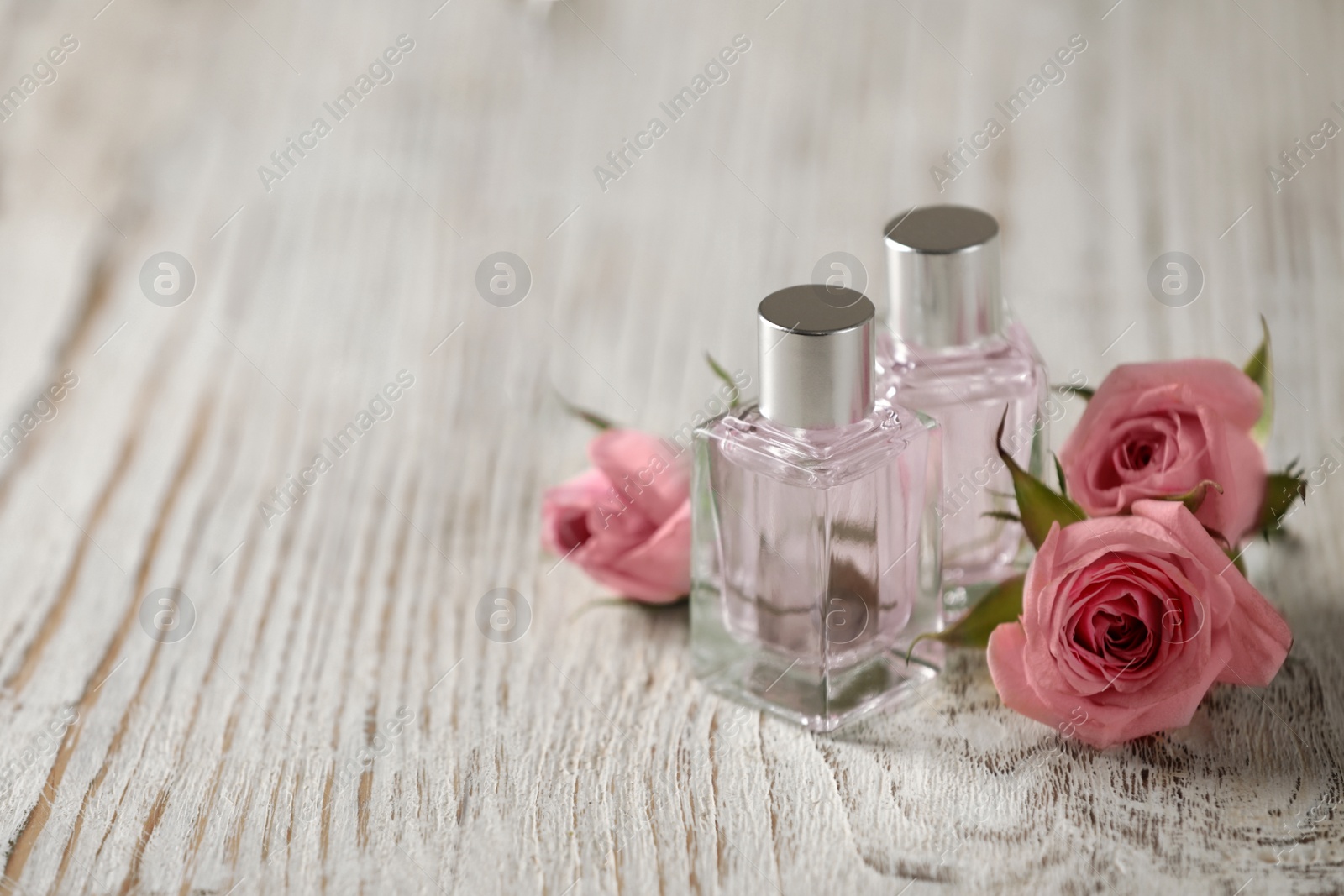 Photo of Bottles of essential oil and roses on white wooden table, space for text