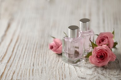 Photo of Bottles of essential oil and roses on white wooden table, space for text