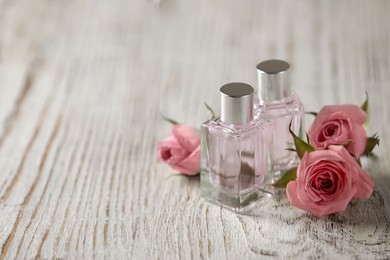 Bottles of essential oil and roses on white wooden table, space for text