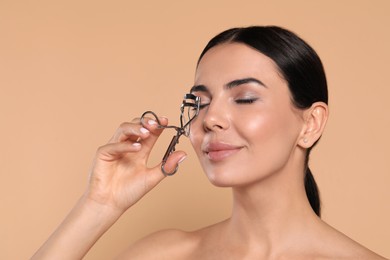 Photo of Beautiful young woman using eyelash curler on beige background