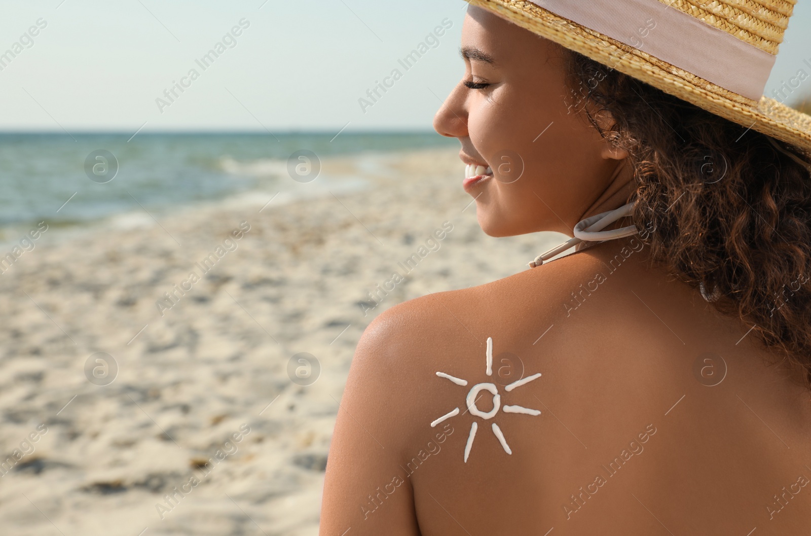 Photo of Beautiful African American woman with sun protection cream on shoulder at beach