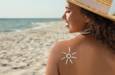 Photo of Beautiful African American woman with sun protection cream on shoulder at beach