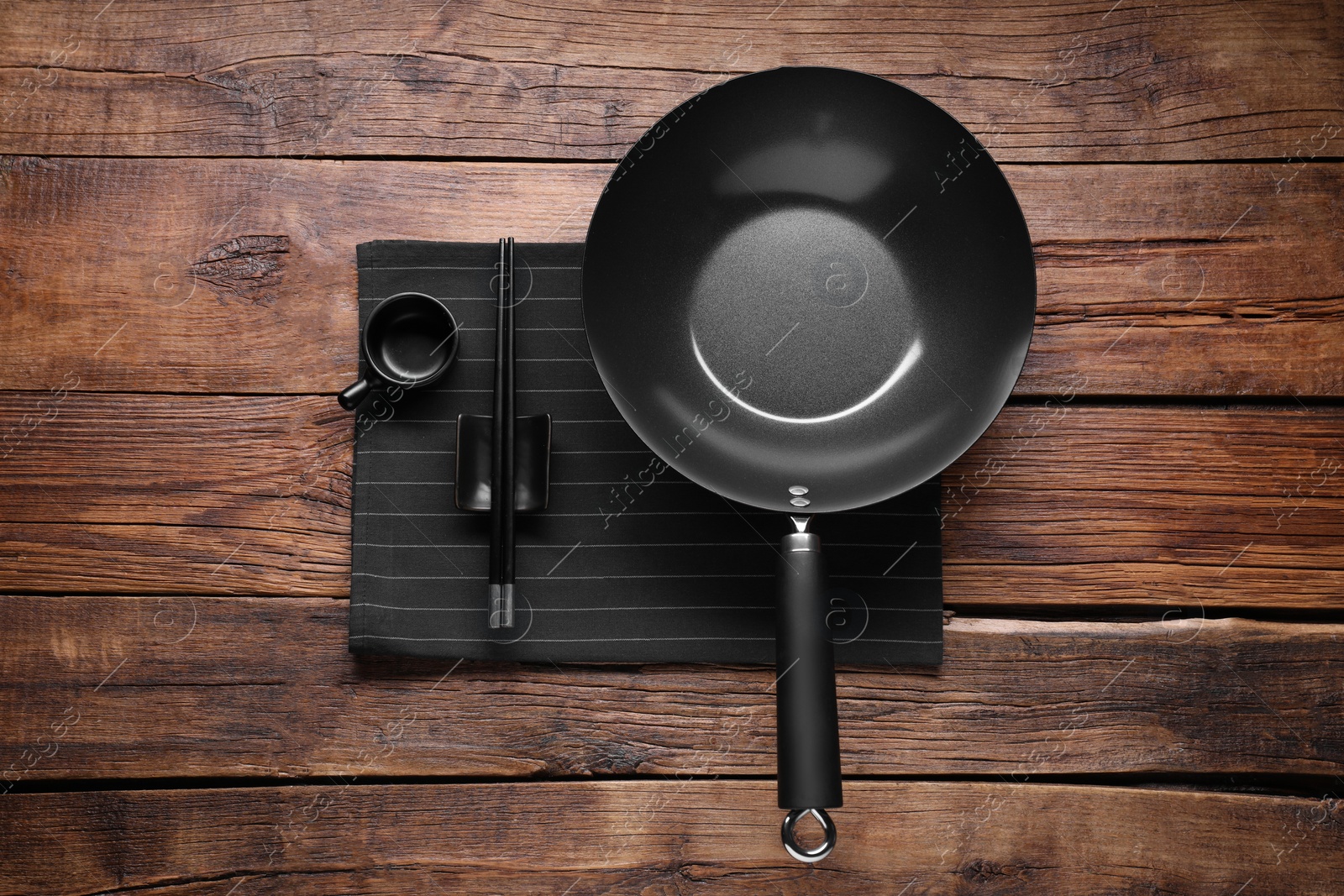 Photo of Empty iron wok, sauce bowl and chopsticks on wooden table, flat lay