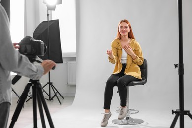 Photo of Casting call. Woman performing while camera operator filming her against light grey background in studio