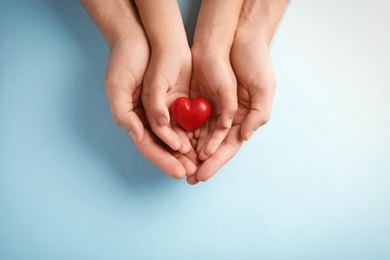 Photo of Family holding small red heart in hands on color background
