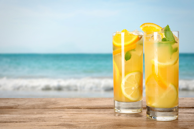 Glasses of refreshing lemonade on wooden table near sea, space for text