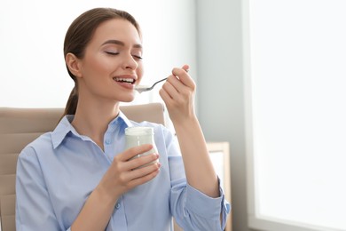Photo of Young attractive woman eating tasty yogurt in office