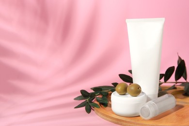 Cosmetic products and olives on pink background, space for text