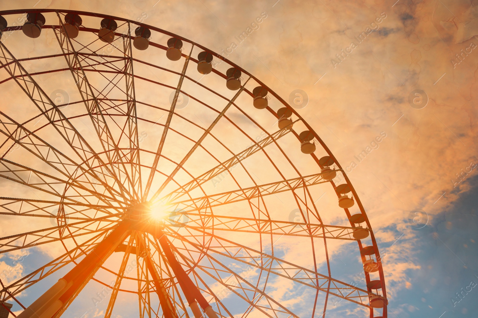 Image of Beautiful large Ferris wheel against blue cloudy sky on sunny day, low angle view