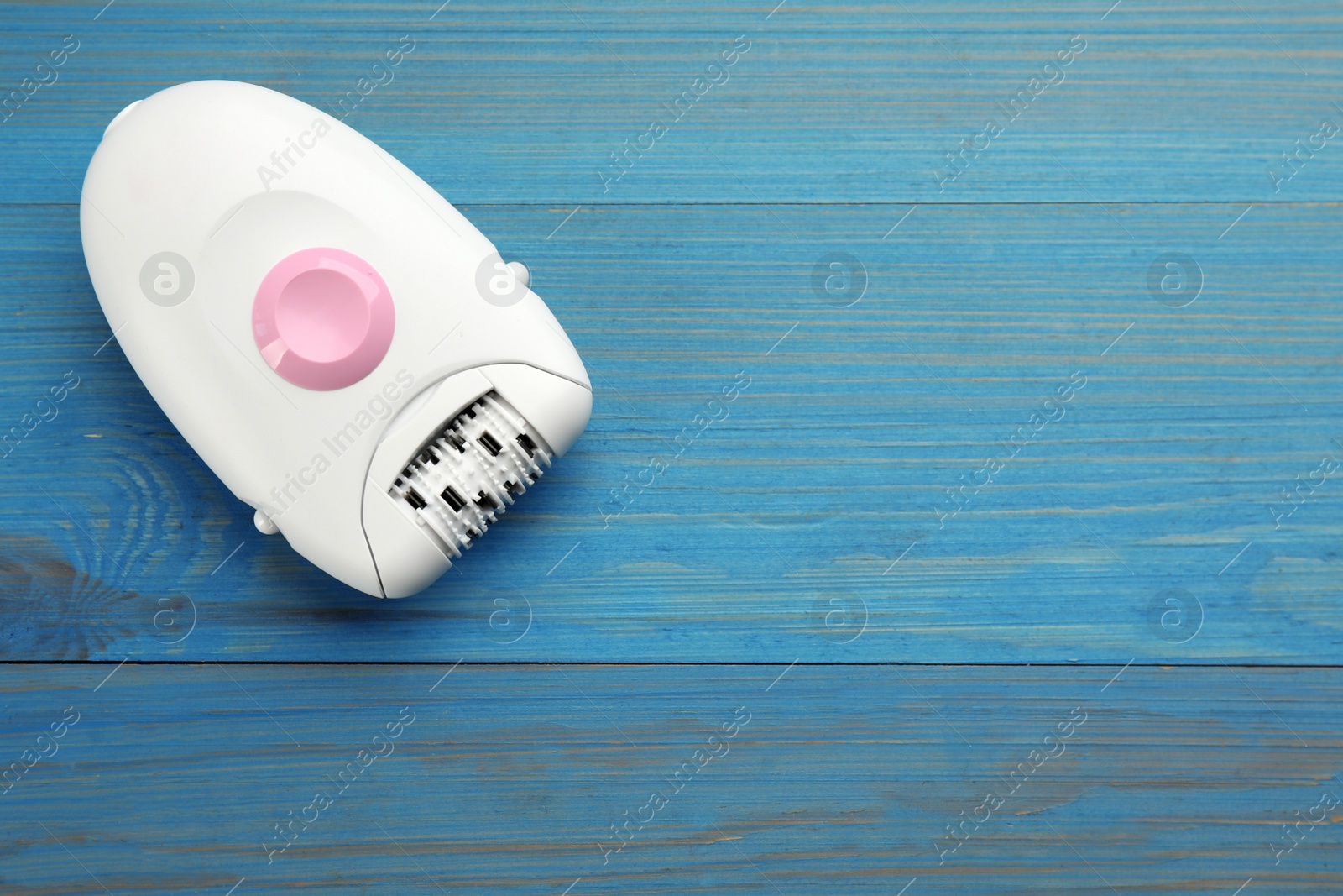 Photo of Modern epilator on light blue wooden table, top view. Space for text