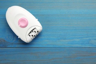 Photo of Modern epilator on light blue wooden table, top view. Space for text