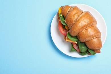 Tasty vegetarian croissant sandwich on light blue background, top view. Space for text