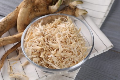 Photo of Grated horseradish and roots on grey wooden table, closeup