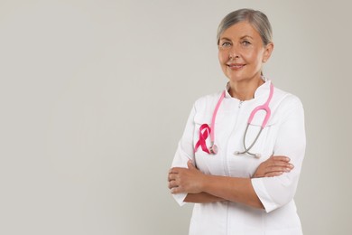 Photo of Doctor with pink ribbon and stethoscope on light grey background, space for text. Breast cancer awareness