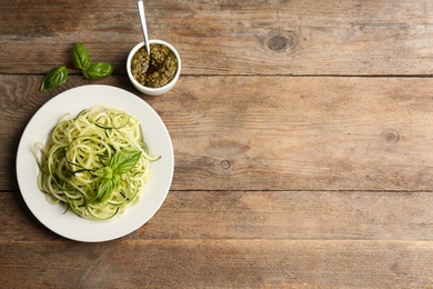 Photo of Delicious zucchini pasta with basil and pesto sauce served on wooden table, flat lay. Space for text